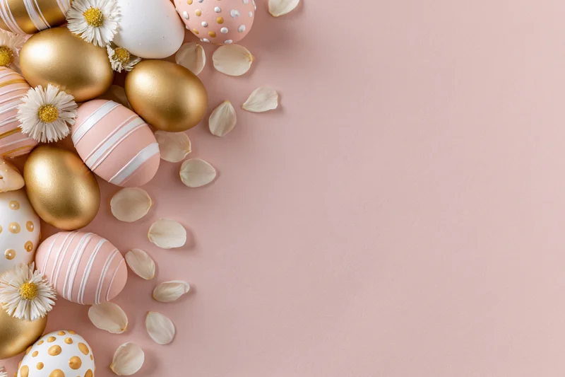 Decorated easter eggs and small white daisies arranged in a border on a pink surface with copyspace