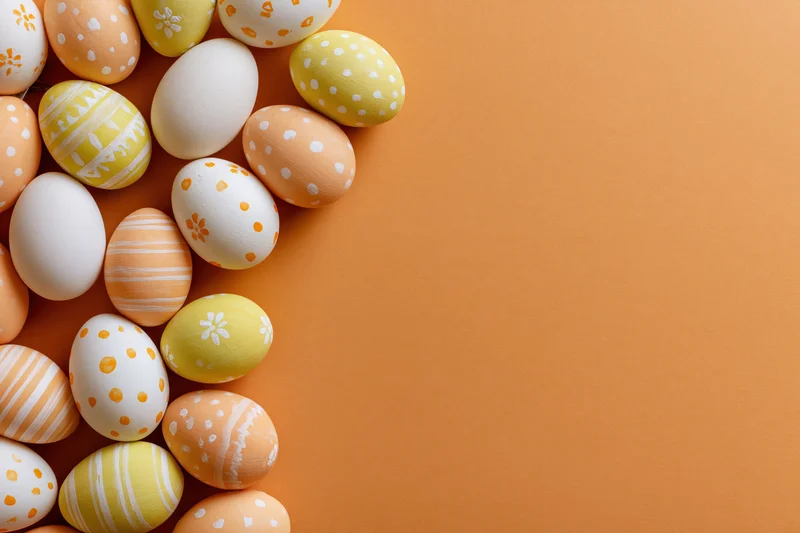 Decorated easter eggs arranged in a loose vertical cluster along the left side of an orange background with copyspace on the right