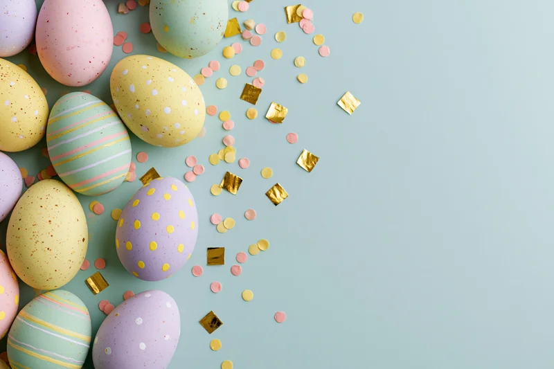 Decorated easter eggs in pastel colors arranged with gold confetti on a light blue surface