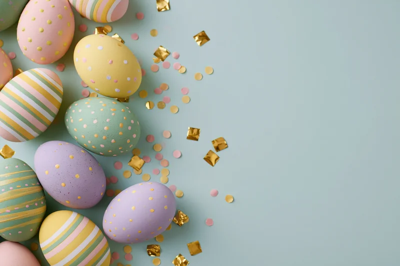 Decorated easter eggs in pastel colors arranged with golden confetti on a light blue surface
