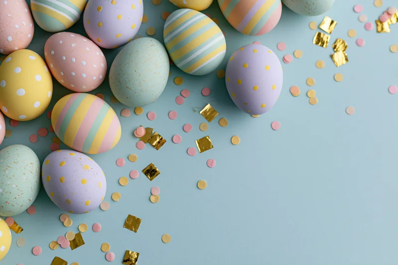 Decorated easter eggs in pastel colors arranged with confetti on a light blue surface