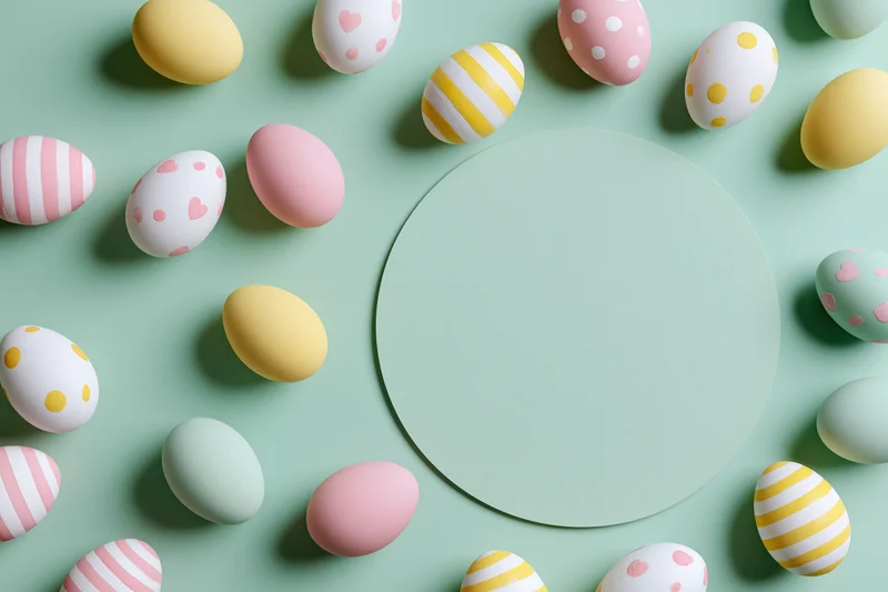 Decorated easter eggs in pastel colors arranged around a circular copyspace on mint background