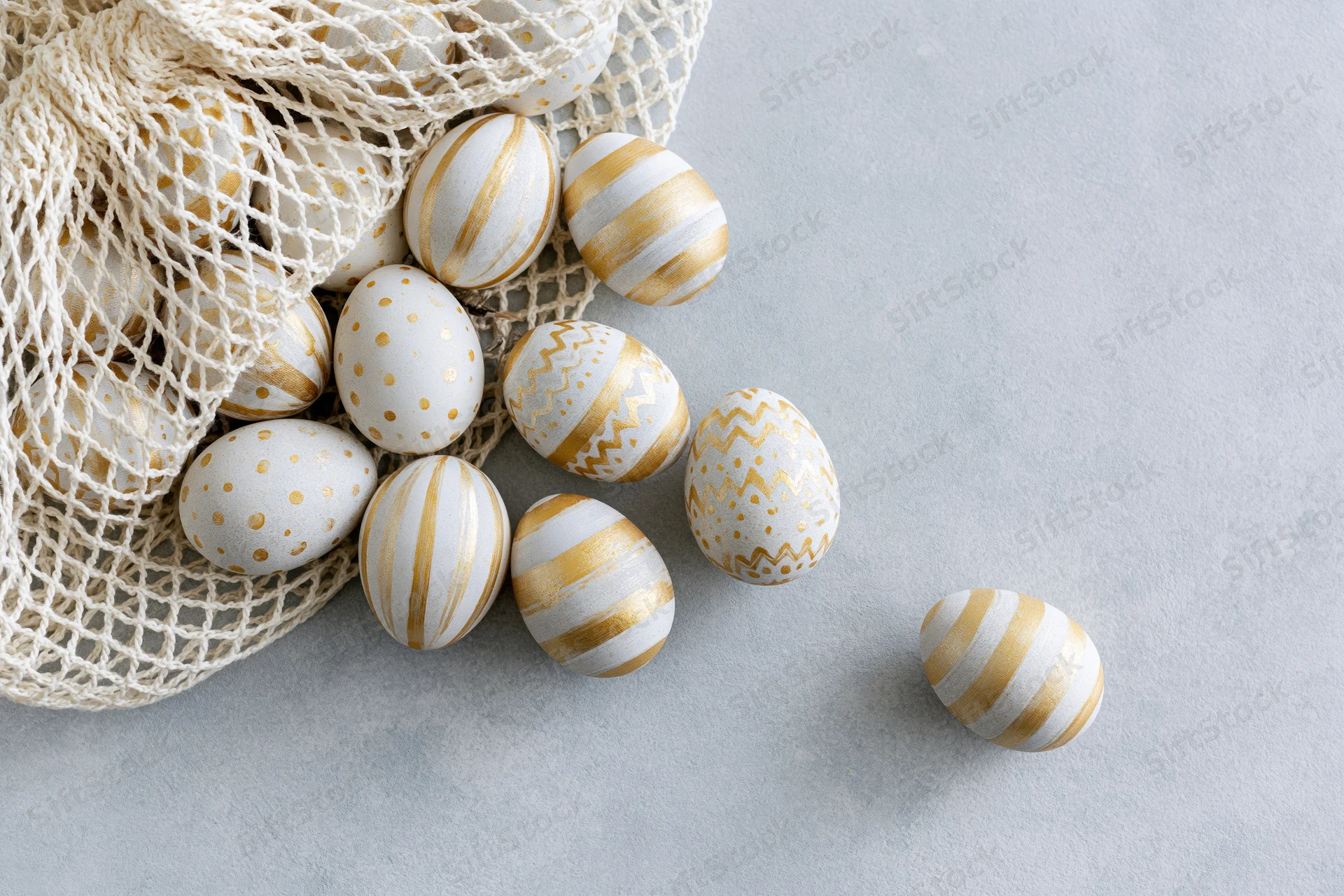 Decorated easter eggs in white and gold patterns spilling from a mesh bag onto a light surface