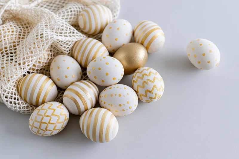 Decorated easter eggs in white and gold patterns arranged on a light surface with a mesh bag and copyspace