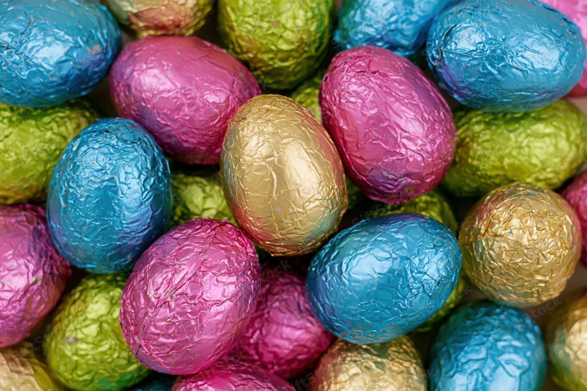 Foil-wrapped chocolate easter eggs piled together in a close-up view