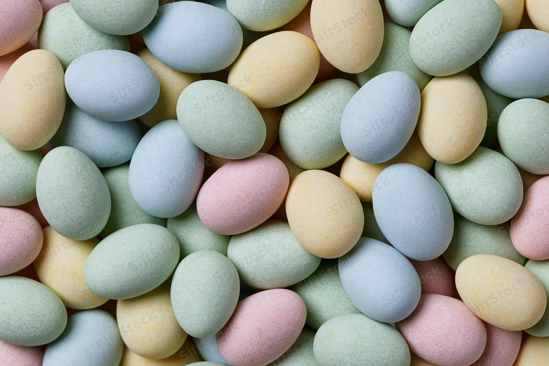 Small pastel candy-coated chocolate eggs densely arranged in a flat lay view