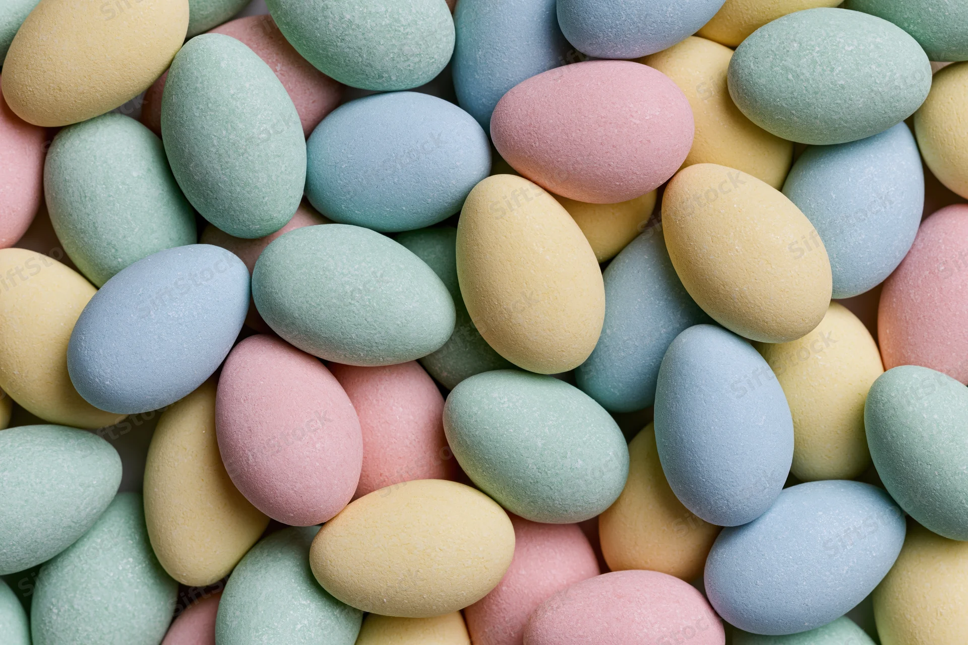Small pastel candy-coated chocolate eggs piled closely together filling the frame