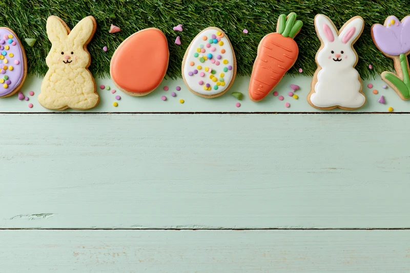 Decorated easter sugar cookies arranged in a row along a grassy edge on a mint wooden surface with copyspace below