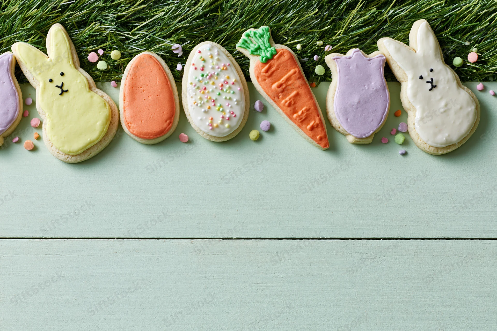Easter-themed decorated sugar cookies arranged in a row along a grassy edge on a mint wooden surface with copyspace below