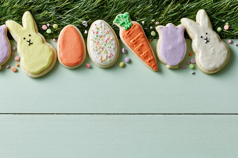 Easter-themed decorated sugar cookies arranged in a row along a grassy edge on a mint wooden surface with copyspace below