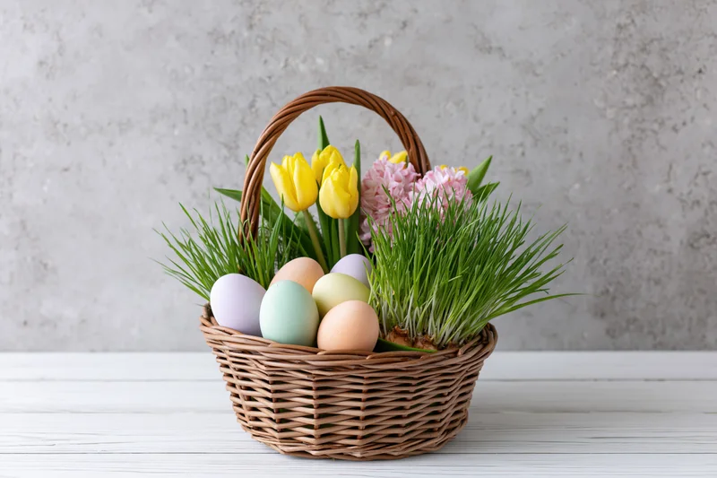 Easter basket with pastel eggs and spring flowers on a white wooden table