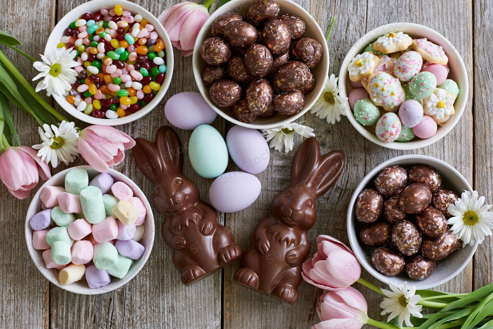 Easter candy spread with chocolate bunnies, eggs, and flowers arranged on a weathered wooden table