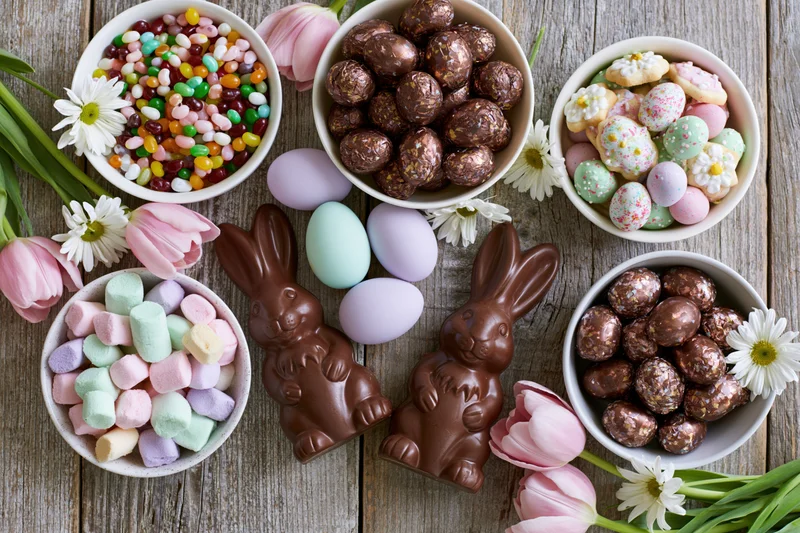 Easter candy spread with chocolate bunnies, eggs, and flowers arranged on a weathered wooden table