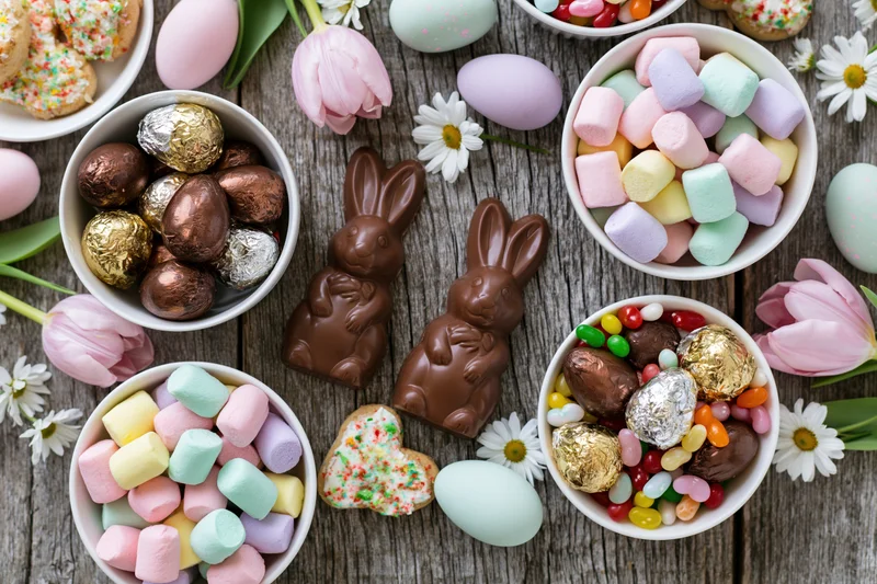 Easter candy spread with chocolate bunnies, marshmallows, eggs and flowers on a weathered wooden table