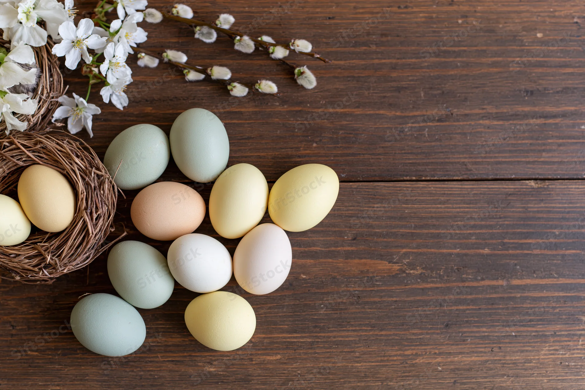 Easter eggs in pastel shades arranged with a nest and blossoms on a dark wooden table