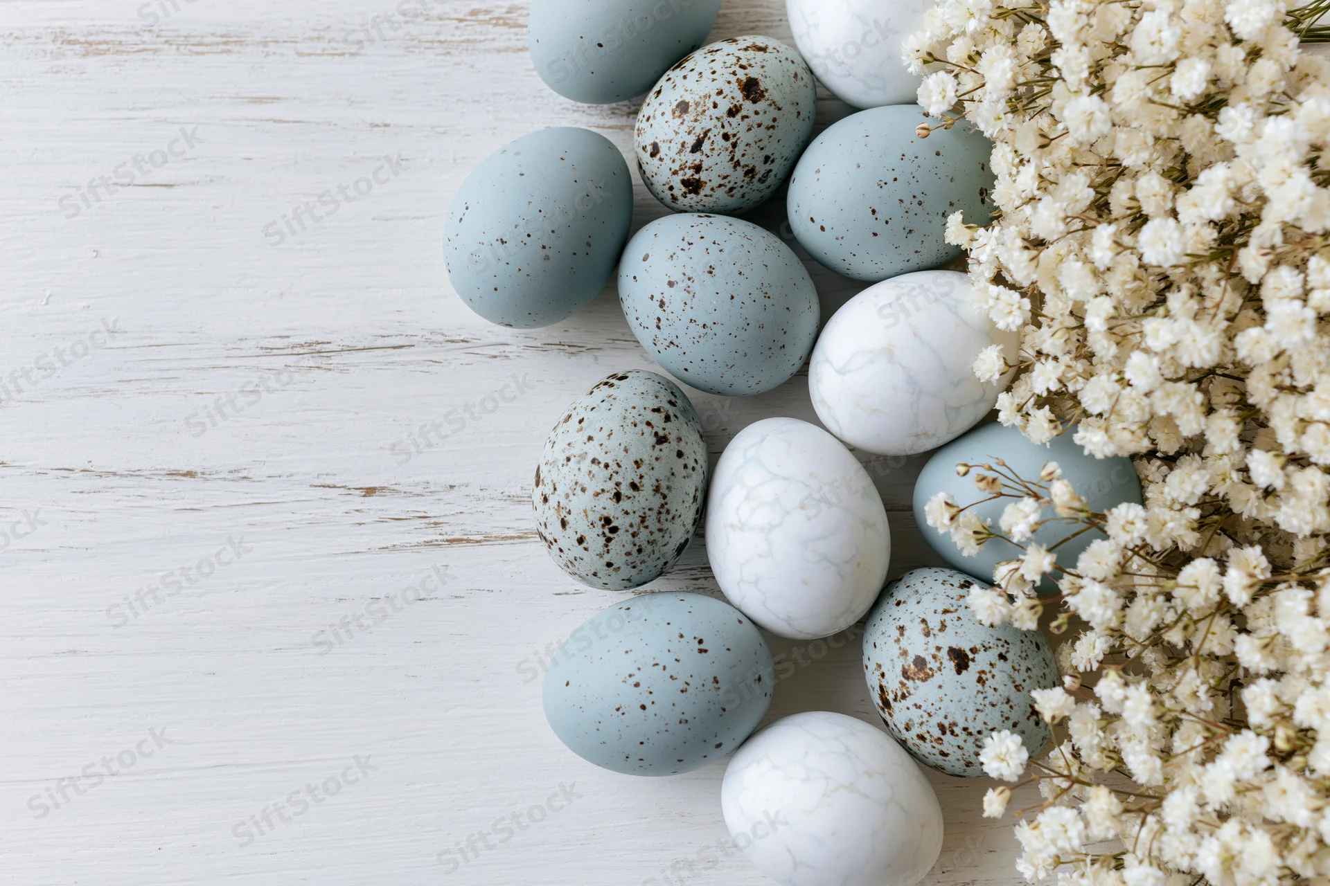 Easter eggs in pale blue and white with speckled and marble patterns arranged with baby's breath flowers on a white wooden surface