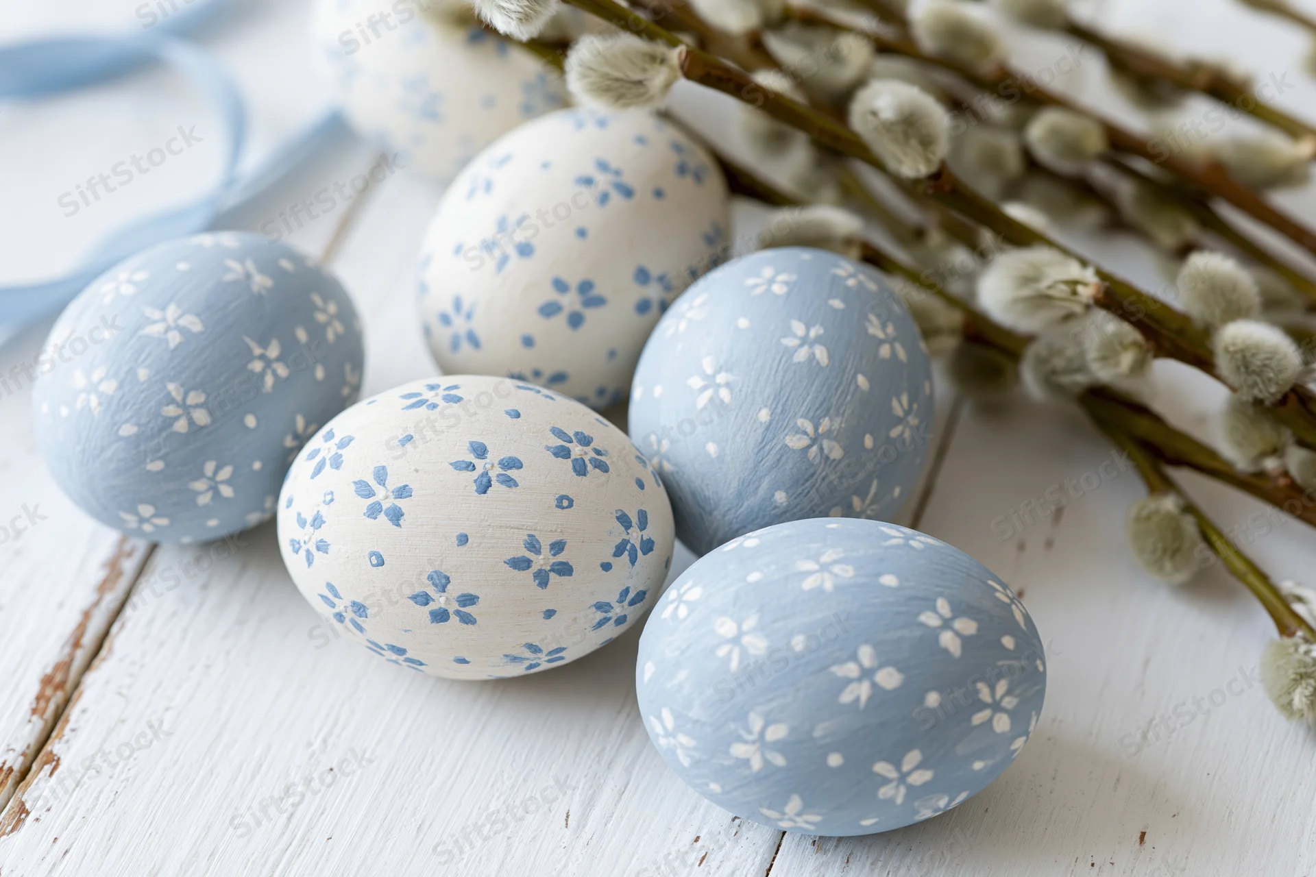 Hand-painted easter eggs with floral patterns arranged on a white wooden surface with willow branches