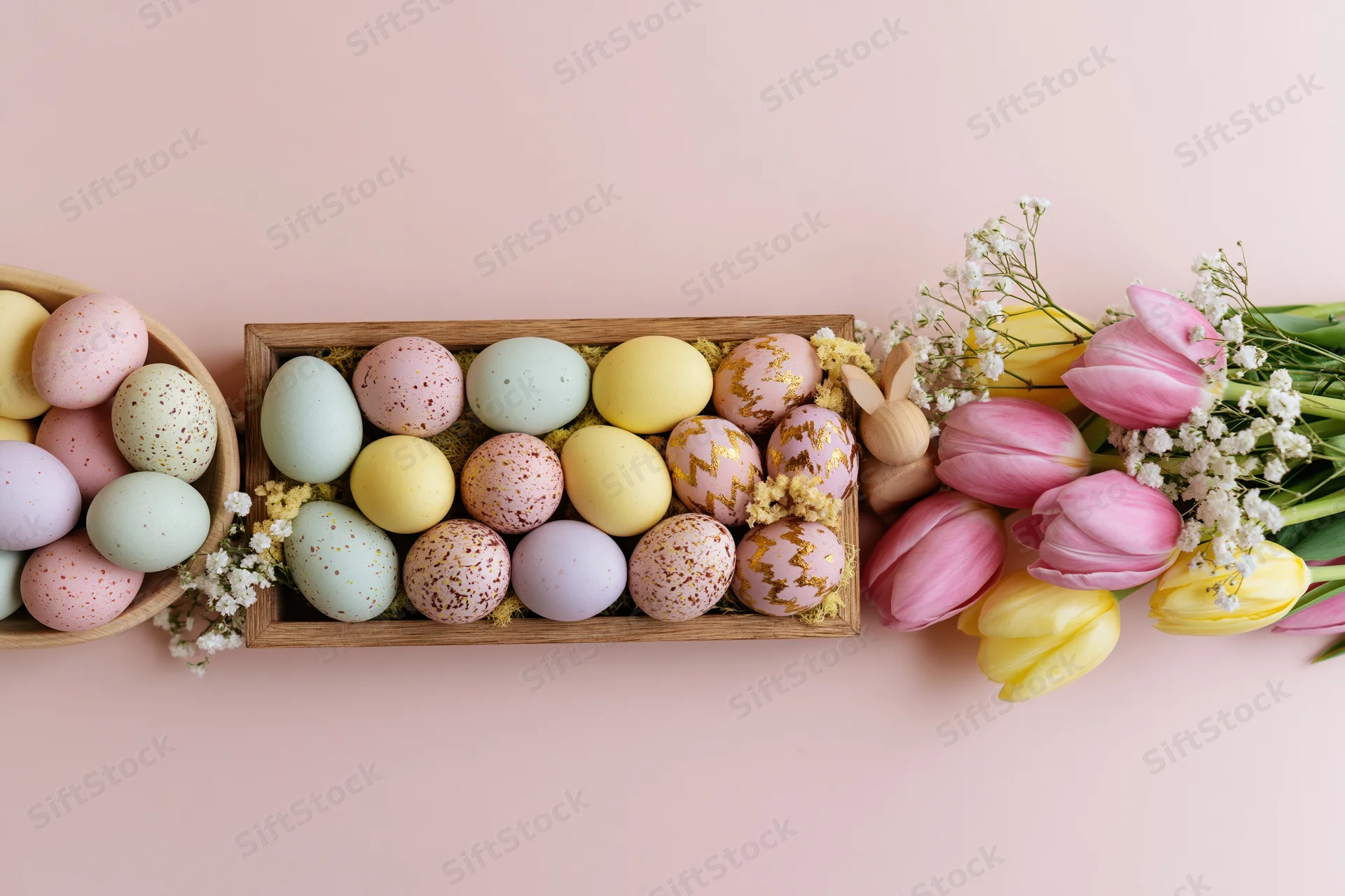Easter eggs and tulips arranged in wooden trays and baskets along the bottom edge of a pale pink surface
