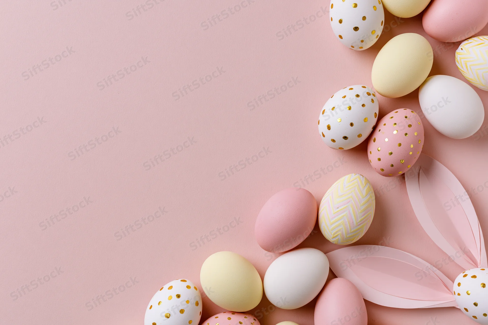 Decorated easter eggs and paper bunny ears arranged in flat lay on pastel pink surface with copyspace