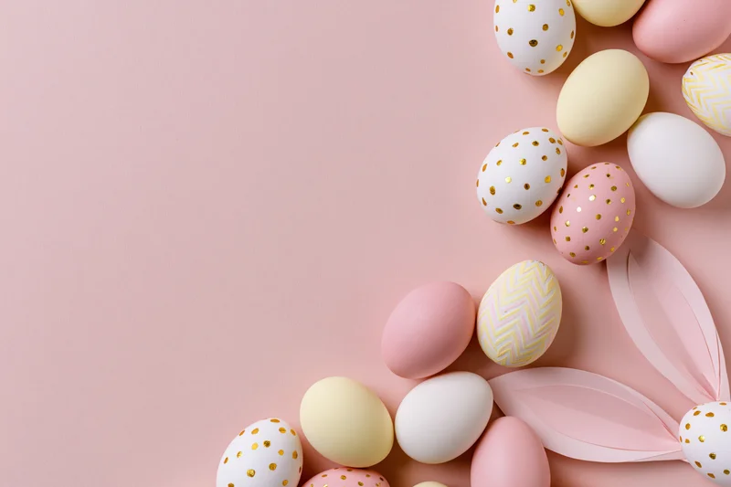 Decorated easter eggs and paper bunny ears arranged in flat lay on pastel pink surface with copyspace