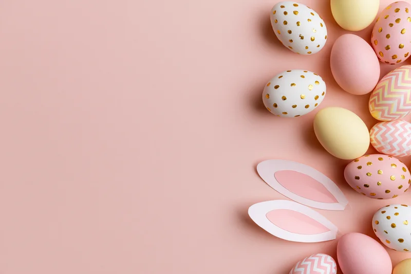 Decorated easter eggs and paper bunny ears arranged in flat lay on pastel pink background