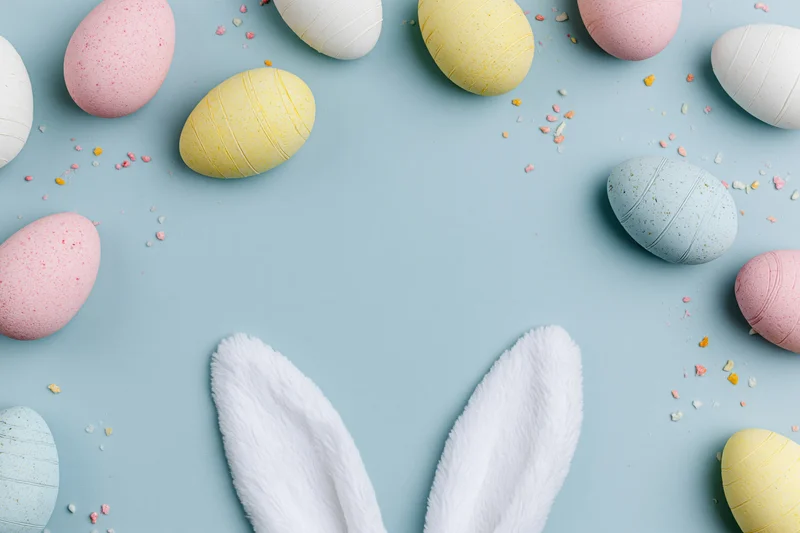 Pastel decorated eggs and bunny ears arranged in flat lay on blue surface with copyspace