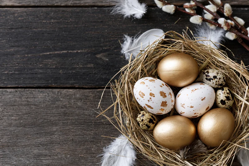 Easter nest with golden and speckled eggs arranged on dark weathered wood surface