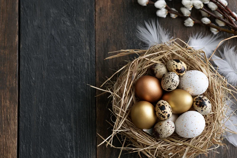 Easter nest with golden and speckled eggs arranged on dark weathered wood surface