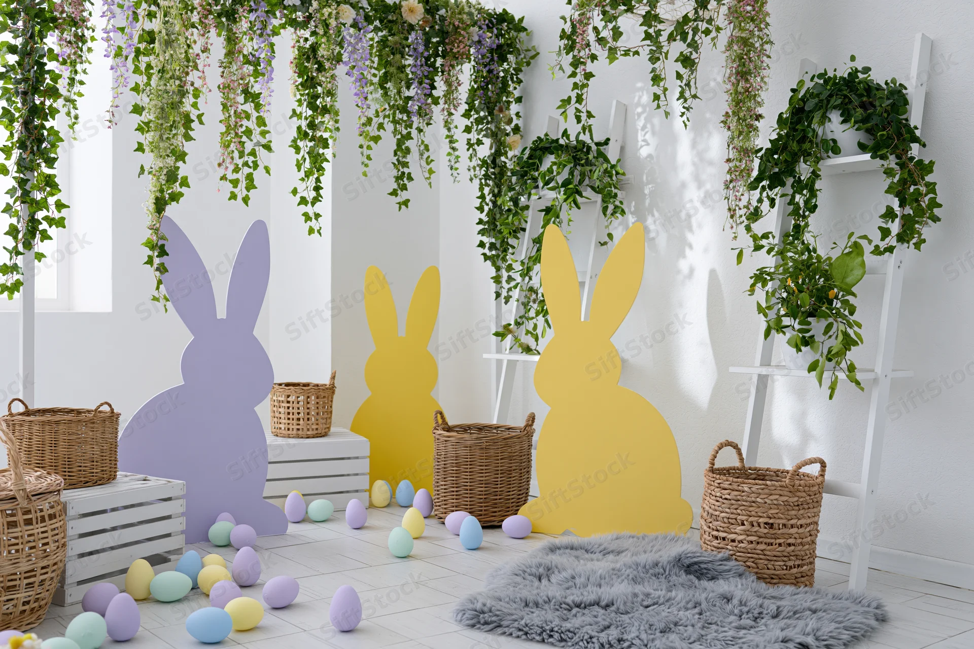 Easter photo booth setup with bunny cutouts, pastel eggs, wicker baskets and hanging greenery in a bright white studio