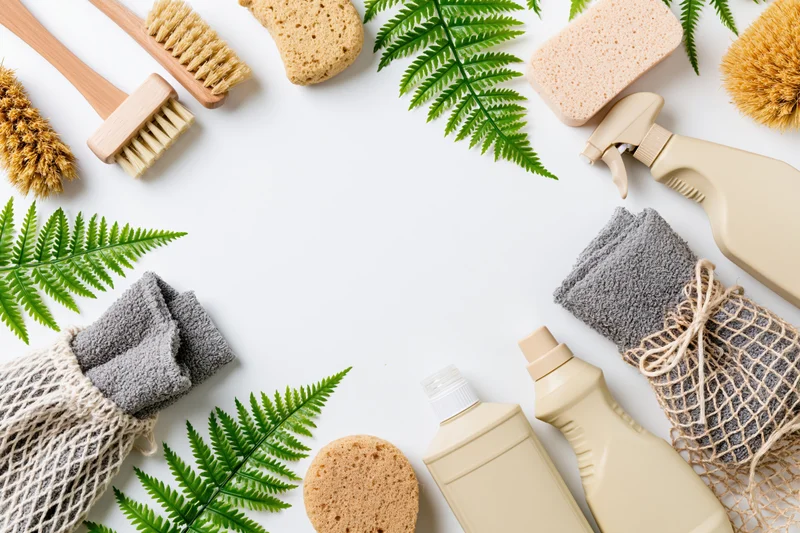 Eco-friendly cleaning supplies arranged in a flat lay frame on white background with fern leaves and copyspace