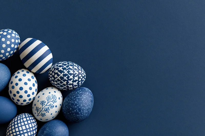 Decorated easter eggs arranged in lower-left corner on blue background with copyspace