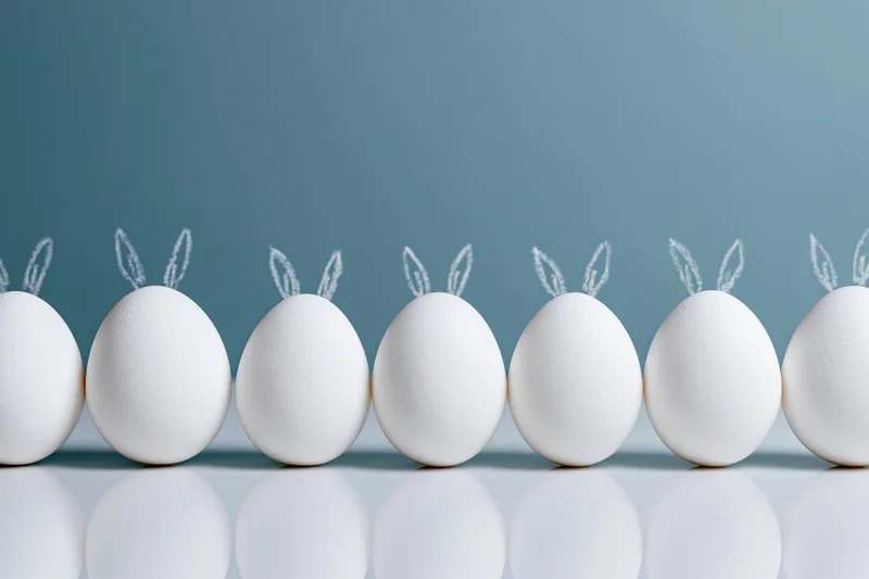 White eggs with bunny ears arranged in a row on a reflective surface
