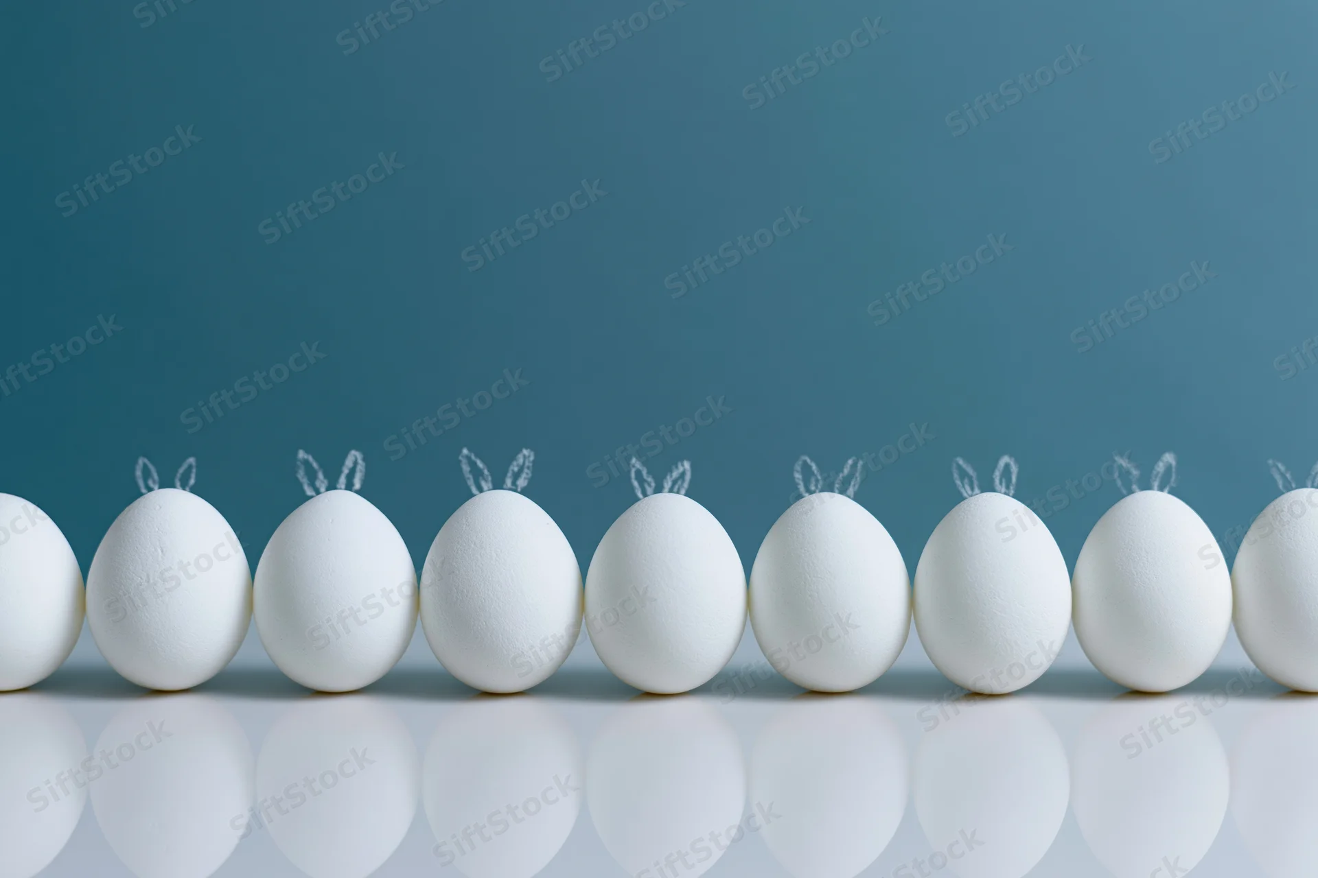 White eggs with bunny ears arranged in a row on a reflective surface