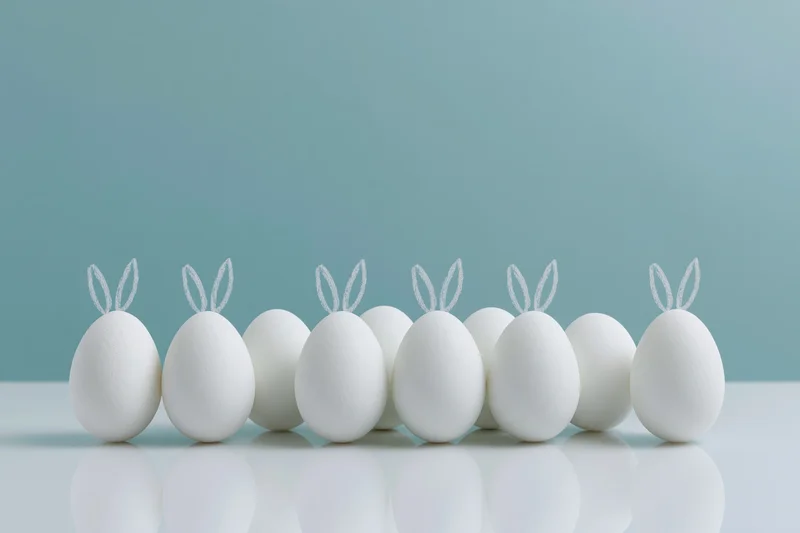 Eight white eggs with bunny ears arranged in a row on a reflective white surface