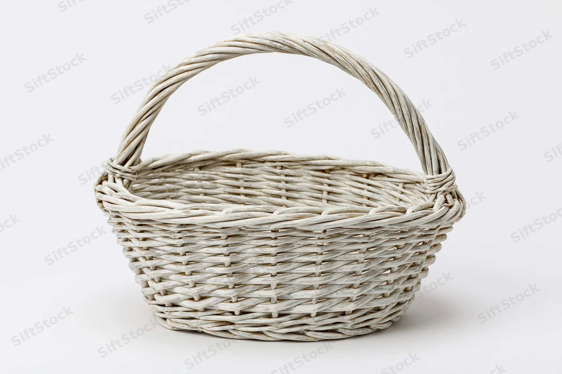 Empty white-painted wicker basket with arched handle on plain white background