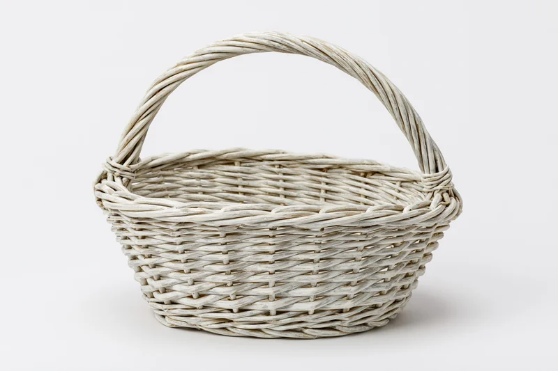 Empty white-painted wicker basket with arched handle on plain white background