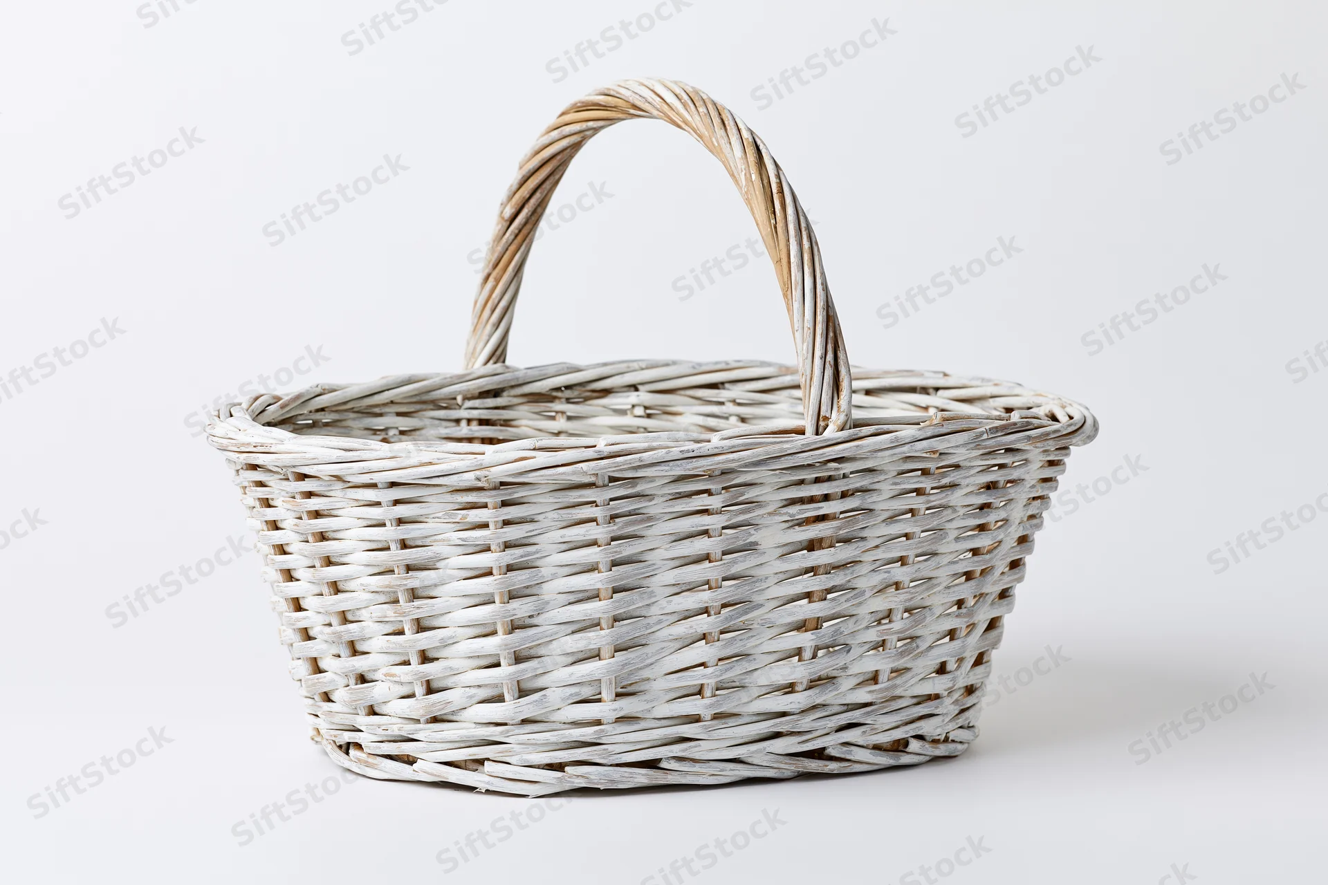 Empty white-painted wicker basket with arched handle on plain white background