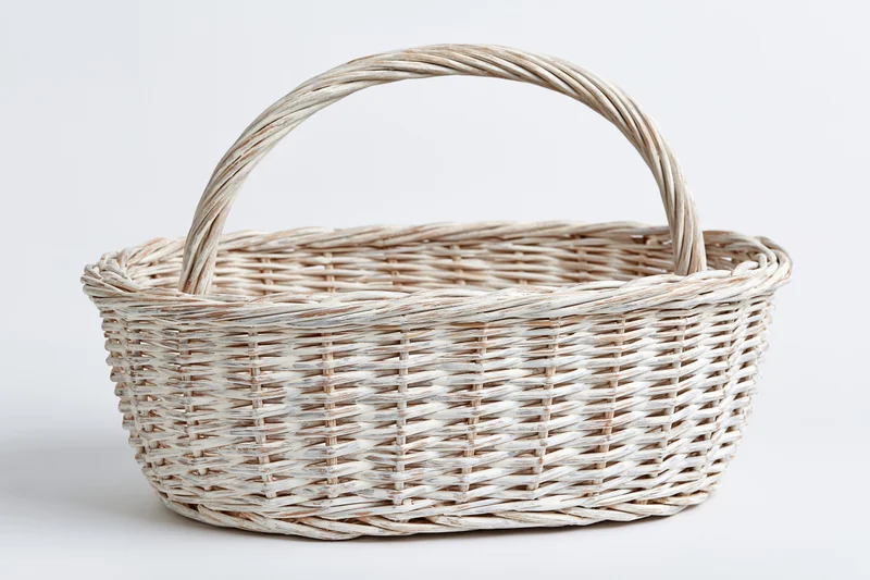 Empty white-painted wicker basket with arched handle on plain white background