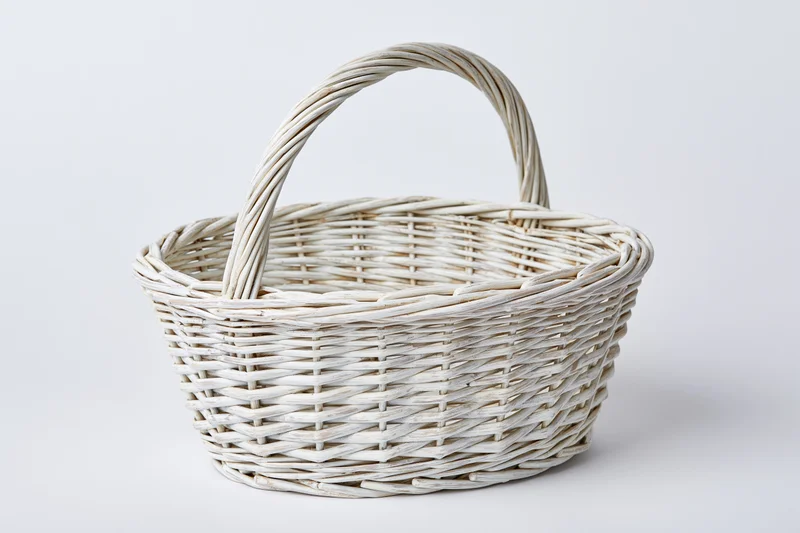Empty white-painted wicker basket with arched handle on plain white background