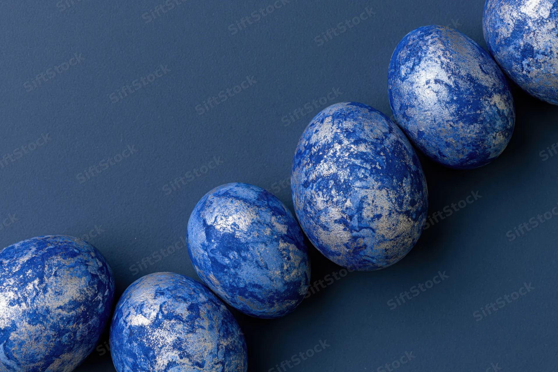 Blue-painted easter eggs with mottled silver and white patterns arranged diagonally on dark surface