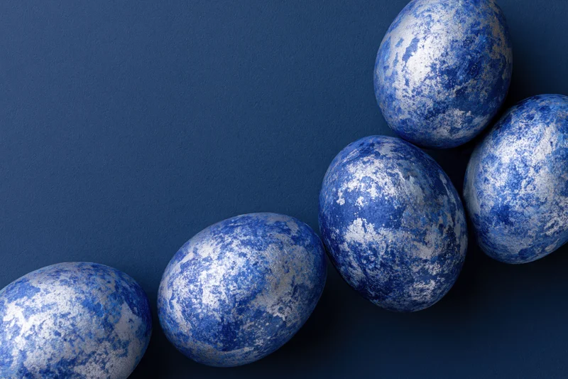 Five blue-painted easter eggs with mottled silver and white pattern arranged diagonally on dark blue background