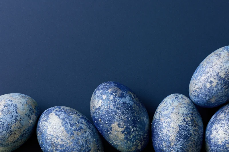 Five blue-painted easter eggs with mottled silver and white finish arranged in a row on a dark blue background with copyspace above