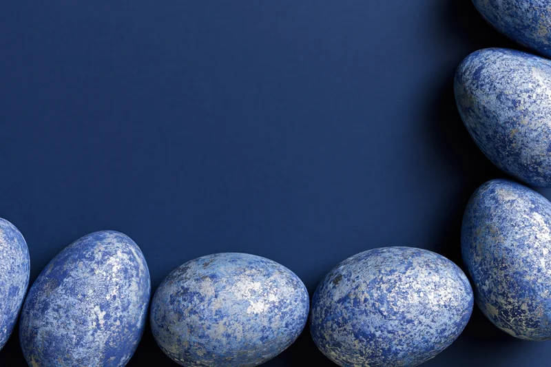 Blue mottled easter eggs arranged in a border on a dark blue surface with copyspace