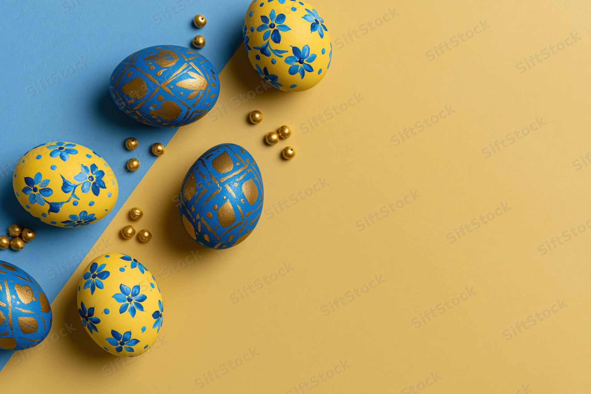 Decorated easter eggs arranged diagonally on a blue and yellow background with gold beads and copyspace