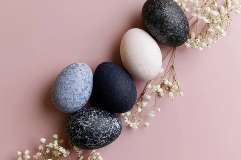 Five marble-painted easter eggs arranged with baby's-breath flowers on a pink surface