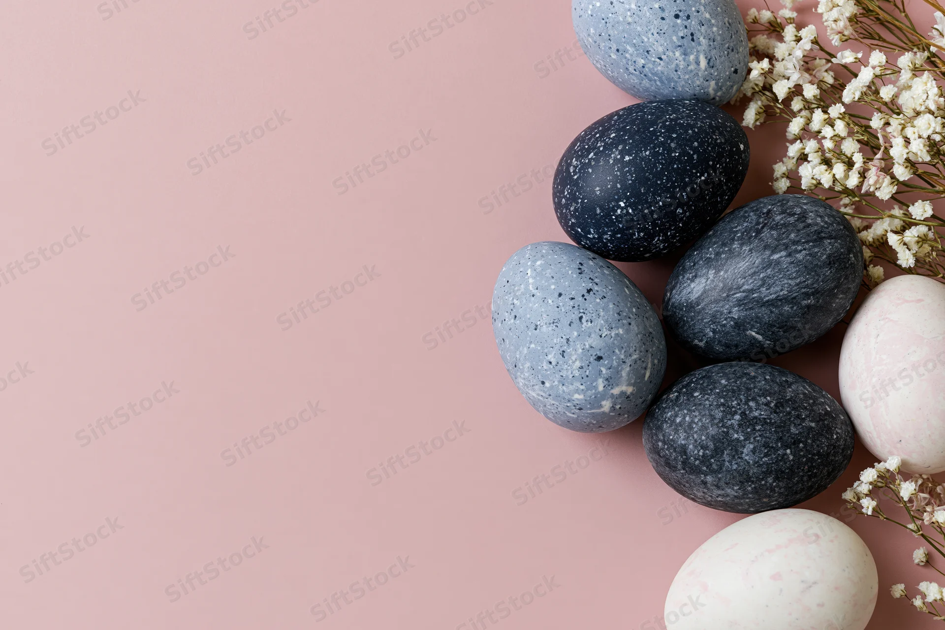 Marble-painted easter eggs arranged with baby's-breath flowers on a pink surface