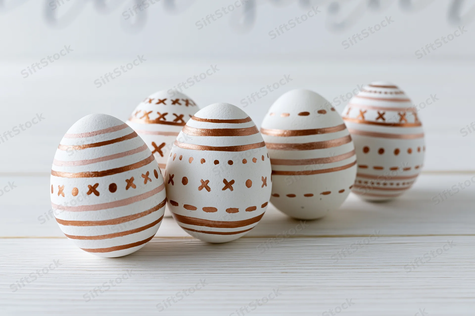 Five white easter eggs with hand-painted copper patterns arranged on a wooden surface