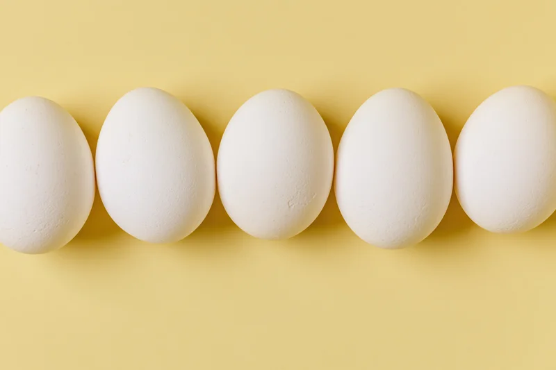 Five white chicken eggs arranged in a horizontal row on a yellow background