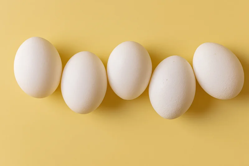 Five white chicken eggs arranged in a loose horizontal row on a yellow background