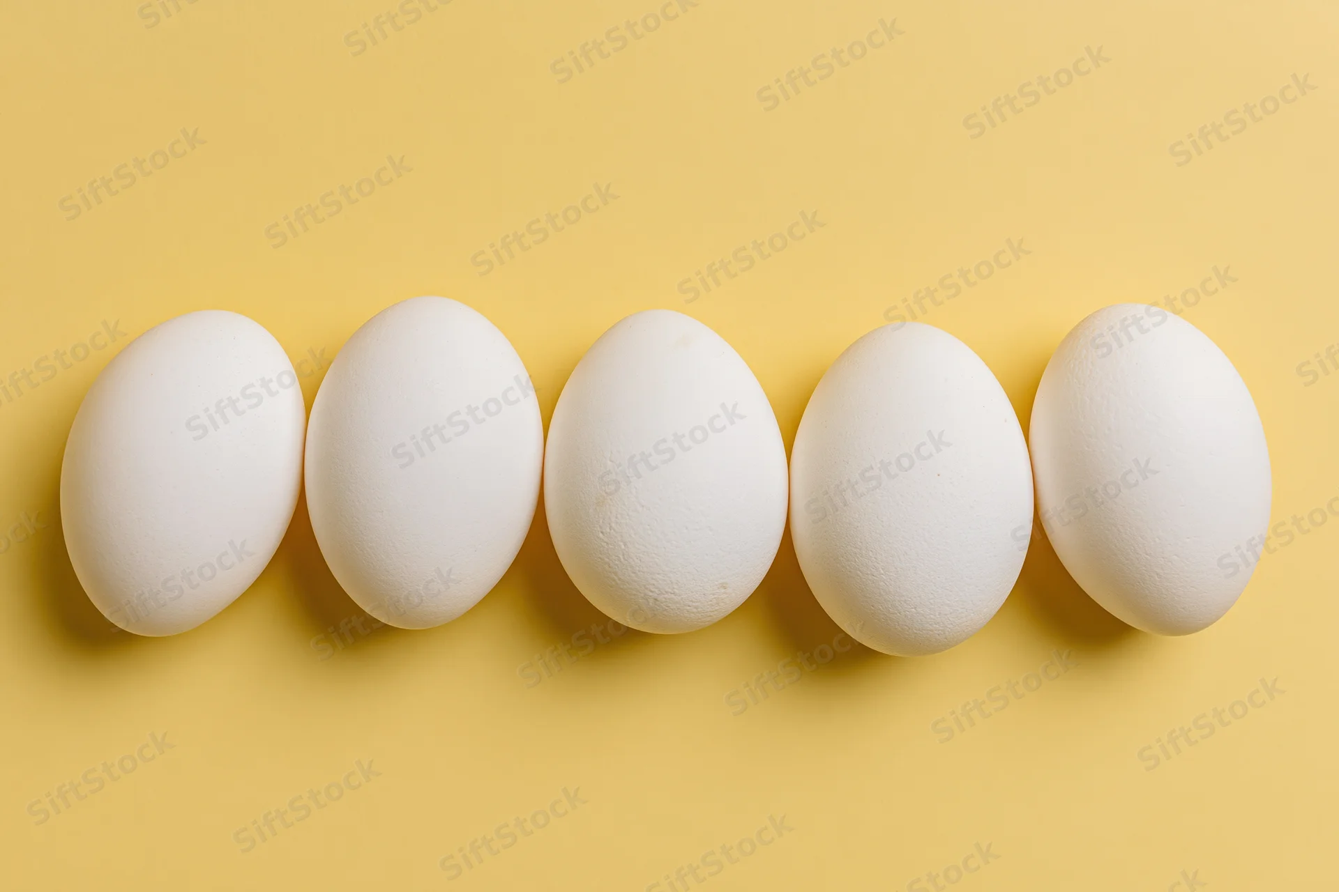 Five white chicken eggs arranged in a loose horizontal row on a yellow background